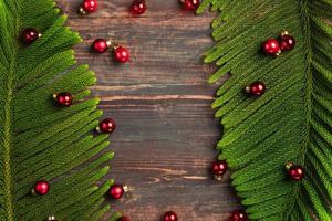 Hoja de pino de Navidad con decoración de adornos rojos sobre mesa de madera