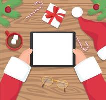 Santa holding tablet on wooden table