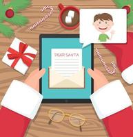Santa claus is sitting at his workplace desk and receiving letter on his tablet from young boy - vector flat design illustration