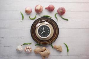 fresh vegetables and alarm clock on heart shape plate on table photo