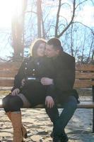 Beautiful happy young couple sitting on the bench in sunny park and making heart gesture together photo