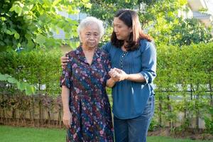 Caregiver help Asian elderly woman while walking with happy in nature park. photo