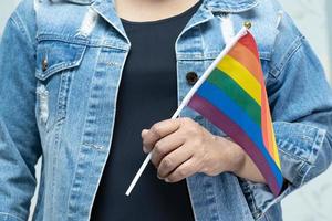 Asian lady wearing blue jean jacket or denim shirt and holding rainbow color flag, symbol of LGBT pride month celebrate annual in June social of gay, lesbian, bisexual, transgender, human rights. photo