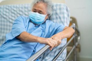 Paciente asiático mayor o anciana con máscara para proteger el coronavirus Acuéstese Manipule la cama de riel con esperanza en una cama en el hospital