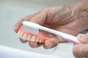 Asian senior or elderly old woman patient use toothbrush to clean partial denture of replacement teeth. photo