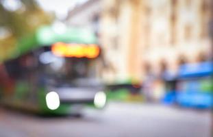 autobús verde defocused borrosa con las luces encendidas en la calle concurrida del centro de la ciudad en un día nublado. Fondo de transporte público de espacio en blanco borroso foto