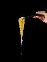 Hand holding chopsticks and noodles on black background photo