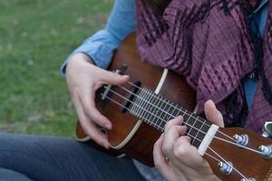 young brunette girl with long hair playing ukulele in the field on the grass