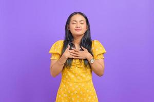 Beautiful young Asian woman put hands on chest on purple background photo