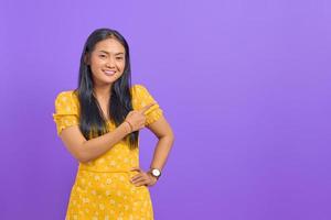 retrato, de, sonriente, joven, mujer asiática, señalar con el dedo, en, espacio de la copia, en, fondo púrpura foto