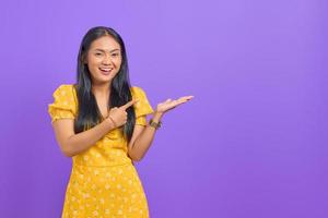 Retrato de mujer asiática joven sonriente que muestra el espacio de la copia en la palma aislada sobre fondo púrpura foto