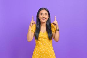 retrato, de, sonriente, joven, mujer asiática, señalar con el dedo, arriba, en, fondo púrpura