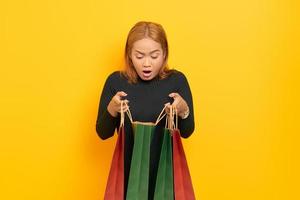 Surprised young Asian woman open shopping bags with open mouth isolated over yellow background photo