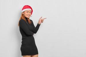 Sonriente joven mujer asiática en santa claus hat señalar con el dedo en el espacio de copia aislado sobre fondo blanco. foto