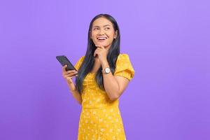 Portrait of smiling young Asian woman using a mobile phone and looking away on purple background photo