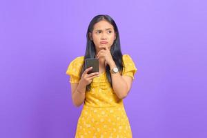 Portrait of pensive young Asian woman using a mobile phone and looking away on purple background photo