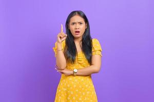 Shocked young Asian woman pointing fingers up and having an idea on purple background photo