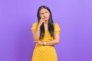 Portrait of pensive young Asian woman looking away at copy space on purple background