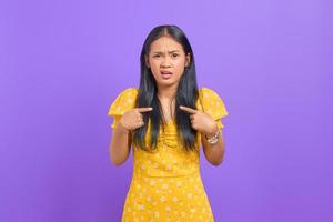 Confused young Asian woman pointing at herself on purple background photo