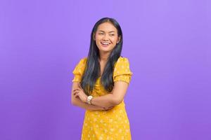 Smiling young Asian woman with crossed arms and looking away on purple background photo