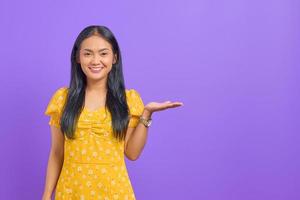 Retrato de mujer asiática joven sonriente que muestra el espacio de la copia en la palma aislada sobre fondo púrpura foto