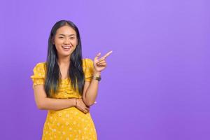 retrato, de, sonriente, joven, mujer asiática, señalar con el dedo, en, espacio de la copia, en, fondo púrpura foto