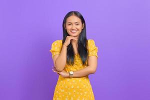 Portrait of smiling young Asian woman raised hand with a crossed arm on purple background photo