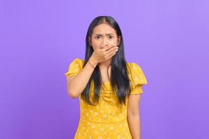 Portrait of shocked young Asian woman covering mouth with hand on purple background photo