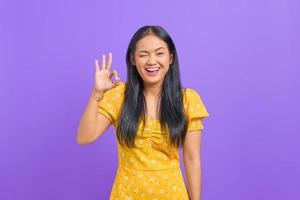 Cheerful young Asian woman makes okay gesture, demonstrates symbol of approval on purple background photo