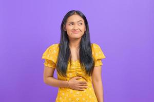 Young Asian woman keep hands on stomach and feel satiety after eating tasty on purple background photo