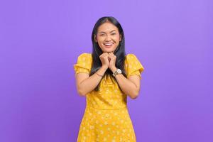 Smiling young Asian woman keeps hand under chin isolated over purple background photo