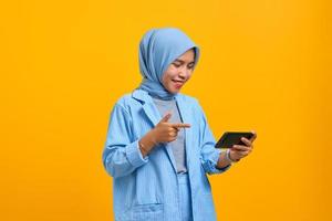 Cheerful young Asian woman playing video game on mobile phone isolated over yellow background photo