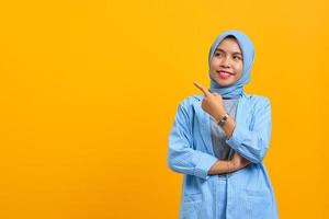 Cheerful young Asian woman pointing fingers aside at copy space isolated over yellow background photo