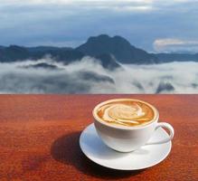 Taza de café con leche en el piso de madera marrón y vistas a la montaña foto