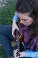 young brunette girl with long hair playing ukulele in the field on the grass
