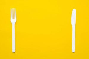 Plastic white fork and knife on yellow background photo