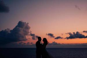 silhouettes of a happy young couple guy and girl on a background of orange sunset photo