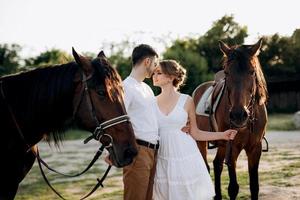 girl in a white sundress and a guy in a white shirt on a walk with brown horses photo