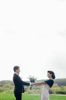 el novio con un traje marrón y la novia con un vestido color marfil en un campo verde foto