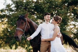 girl in a white sundress and a guy in a white shirt on a walk with brown horses photo