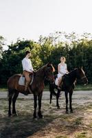 girl in a white sundress and a guy in a white shirt on a walk with brown horses photo