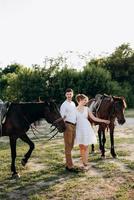 chica con un vestido blanco y un chico con una camisa blanca en un paseo con caballos marrones foto