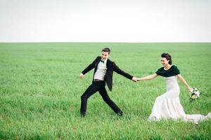 el novio con un traje marrón y la novia con un vestido color marfil en un campo verde foto