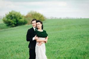 the groom in a brown suit and the bride in an ivory-colored dress on a green field photo