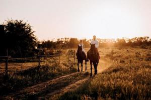 girl in a white sundress and a guy in a white shirt on a walk with brown horses photo