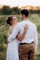 chica con un vestido blanco y un chico con una camisa blanca en un paseo al atardecer con un ramo foto