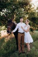 girl in a white sundress and a guy in a white shirt on a walk with brown horses photo