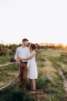 girl in a white sundress and a guy in a white shirt on a walk at sunset with a bouquet photo