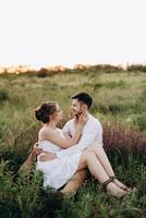 girl in a white sundress and a guy in a white shirt on a walk at sunset with a bouquet photo