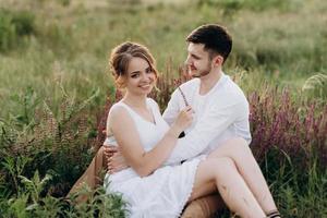 girl in a white sundress and a guy in a white shirt on a walk at sunset with a bouquet photo